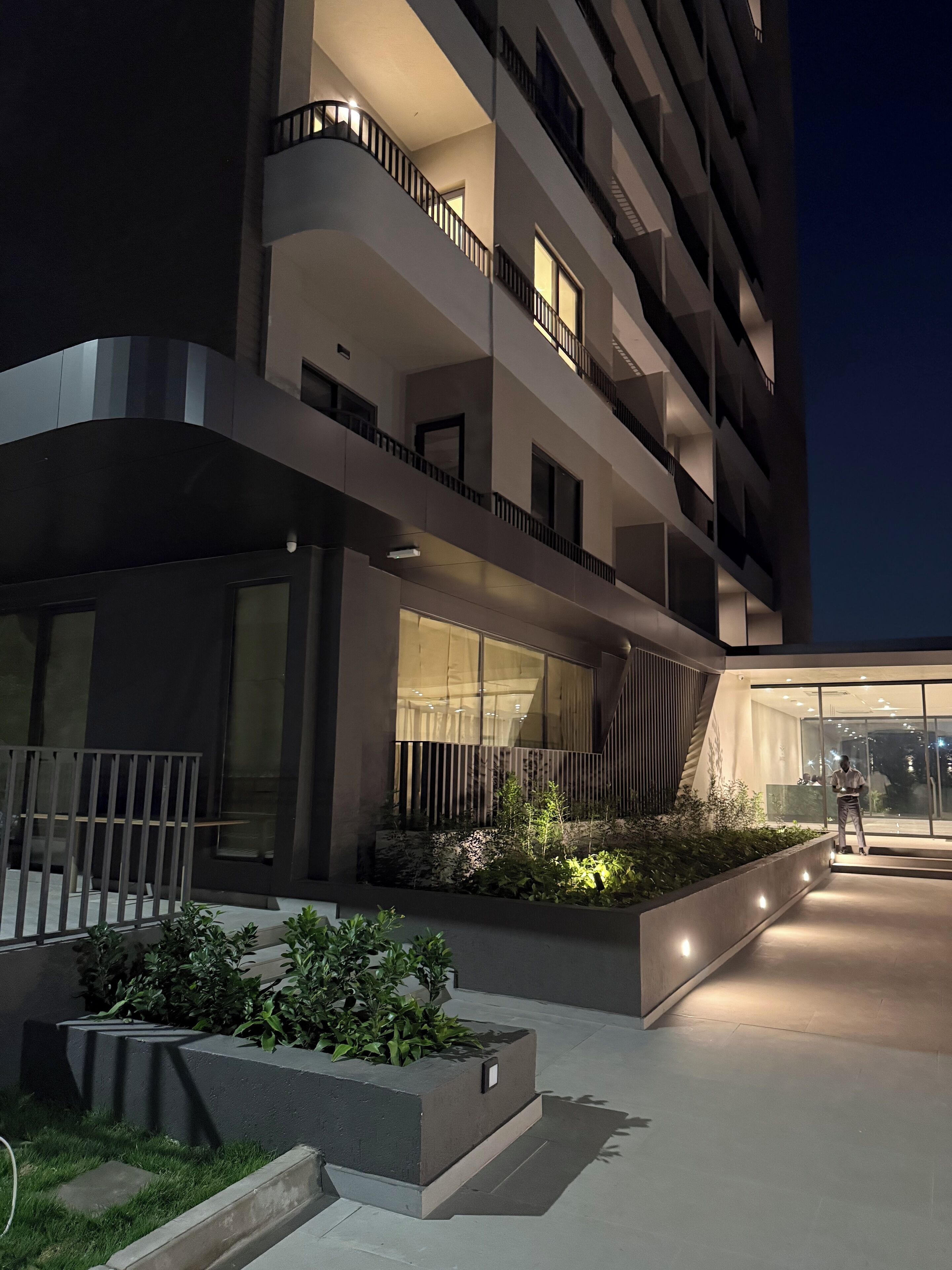 Un immeuble moderne à plusieurs étages, doté de balcons, de grandes fenêtres et d’un espace jardin aménagé.