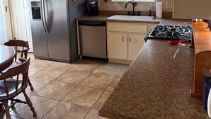 Una cocina con armarios blancos, un refrigerador de acero inoxidable, una estufa a gas y un comedor con sillas de madera.