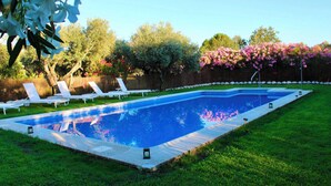 A rectangular swimming pool with a tiled edge, surrounded by a grassy lawn and white lounge chairs.