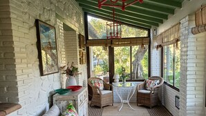 A room with a herringbone floor, a sofa with floral cushions, wicker chairs, a small table, and a hanging red lantern.
