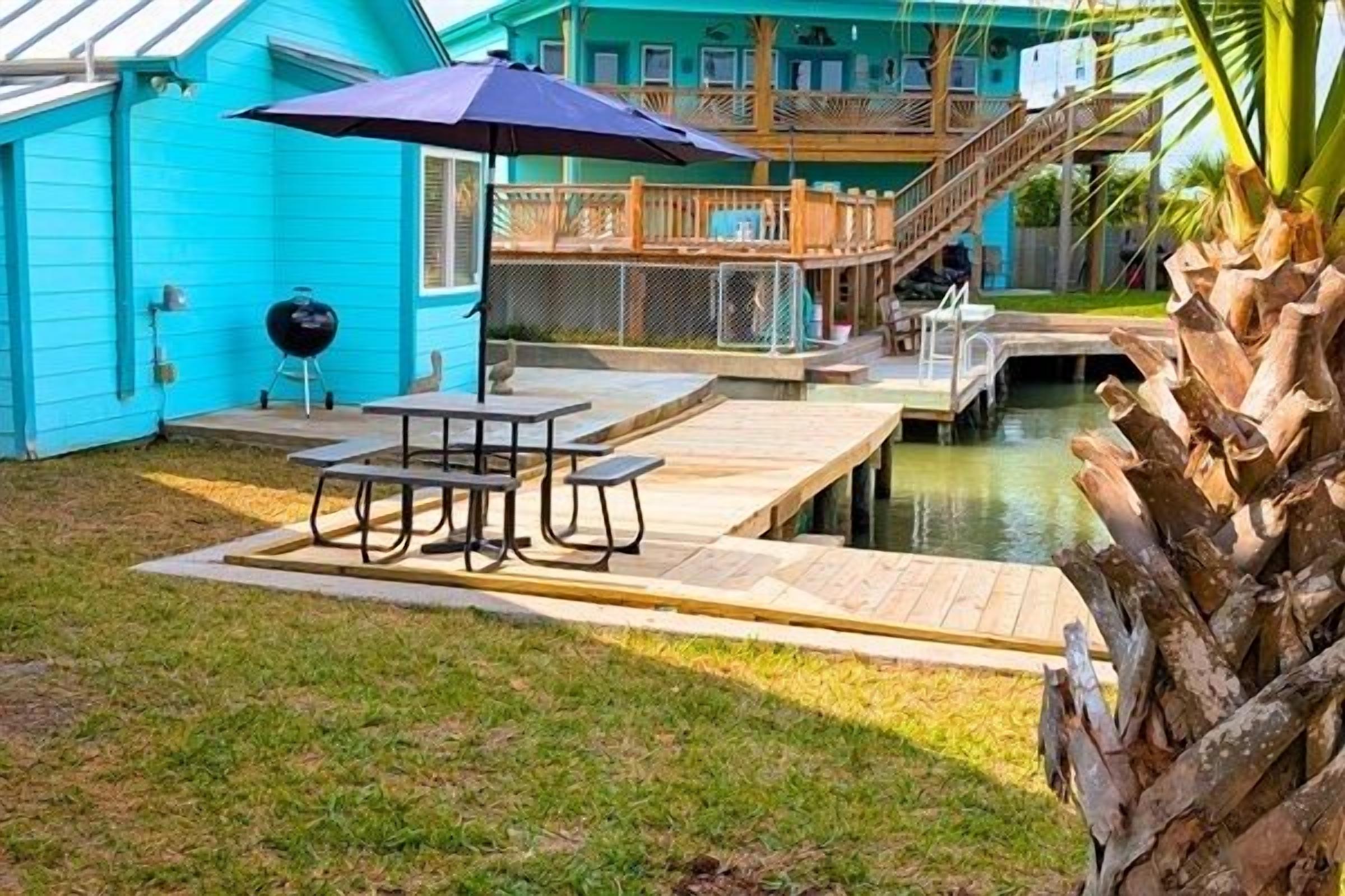 Un jardin avec une terrasse en bois, un barbecue, une table avec des chaises et une petite piscine.