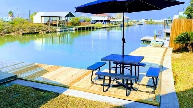 Ein Poolbereich mit Tisch, Sonnenschirm, Holzterrasse und Blick auf das Wasser.