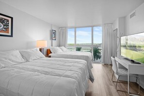 Ein Hotelzimmer mit zwei Betten, einem Schreibtisch mit Fernseher und einem großen Fenster mit Blick ins Freie.