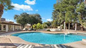 Una piscina con sillas de descanso, rodeada de árboles y una pérgola.