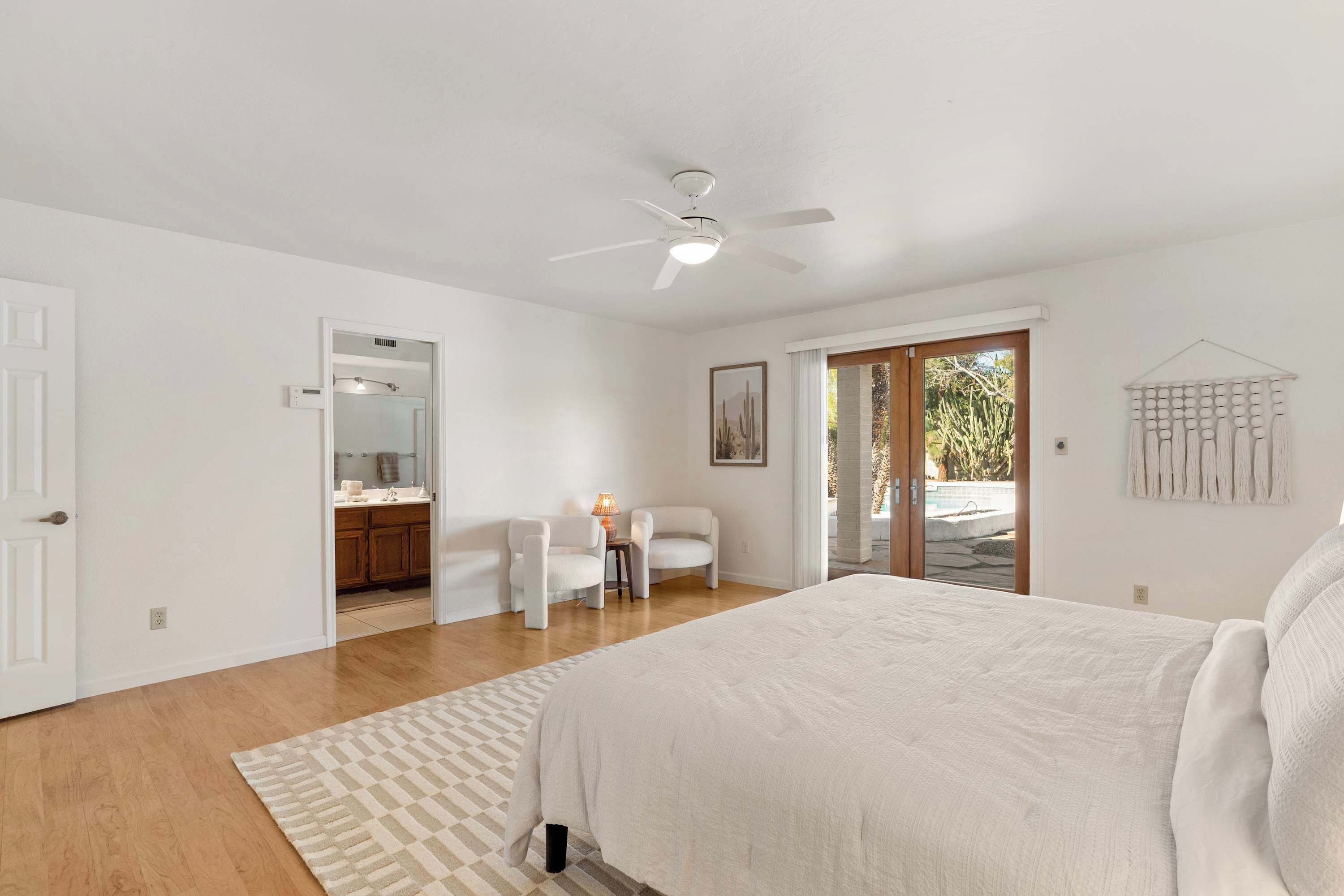 Quarto com cama grande, ventoinha no teto, escrivaninha com cadeira e vista para o exterior através de uma porta de vidro.