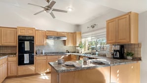 Una cocina moderna con armarios de madera, una isla central con taburetes y un ventilador de techo, además de una cafetera.