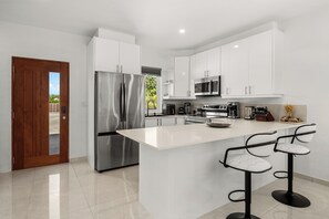 A modern kitchen with white cabinets, stainless steel appliances, and a central island with bar stools. - Twins Villa - Mellizo A - Wonderful 2-bedroom villa with AC in Long Bay Hills (Long Bay Hills)