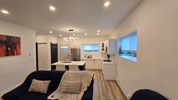 Una sala moderna con un sofá azul oscuro, un plaid color beige y una zona de comedor con una mesa pequeña y sillas.