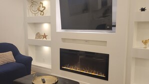 Una sala de estar moderna con un televisor de pantalla plana sobre la chimenea, un sofá azul y estanterías decorativas.
