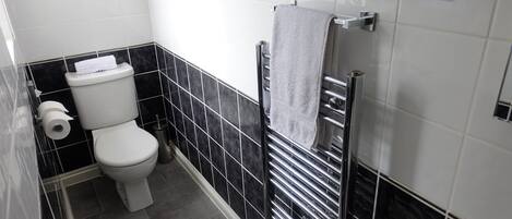 A compact bathroom with a toilet, a towel rack, and a paper towel dispenser.