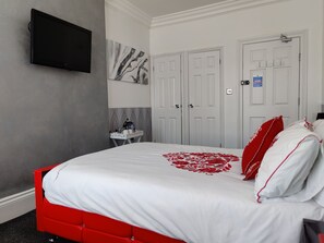Una habitación de hotel con una cama, un televisor de pantalla plana en la pared, un cuadro y un juego de puertas dobles.