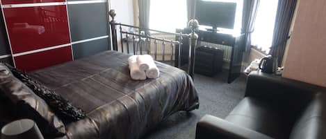 A hotel room with a bed, a desk, a chair, and a television.