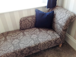 Un sofá de esquina con tela estampada, un cojín azul y una ventana con persianas.