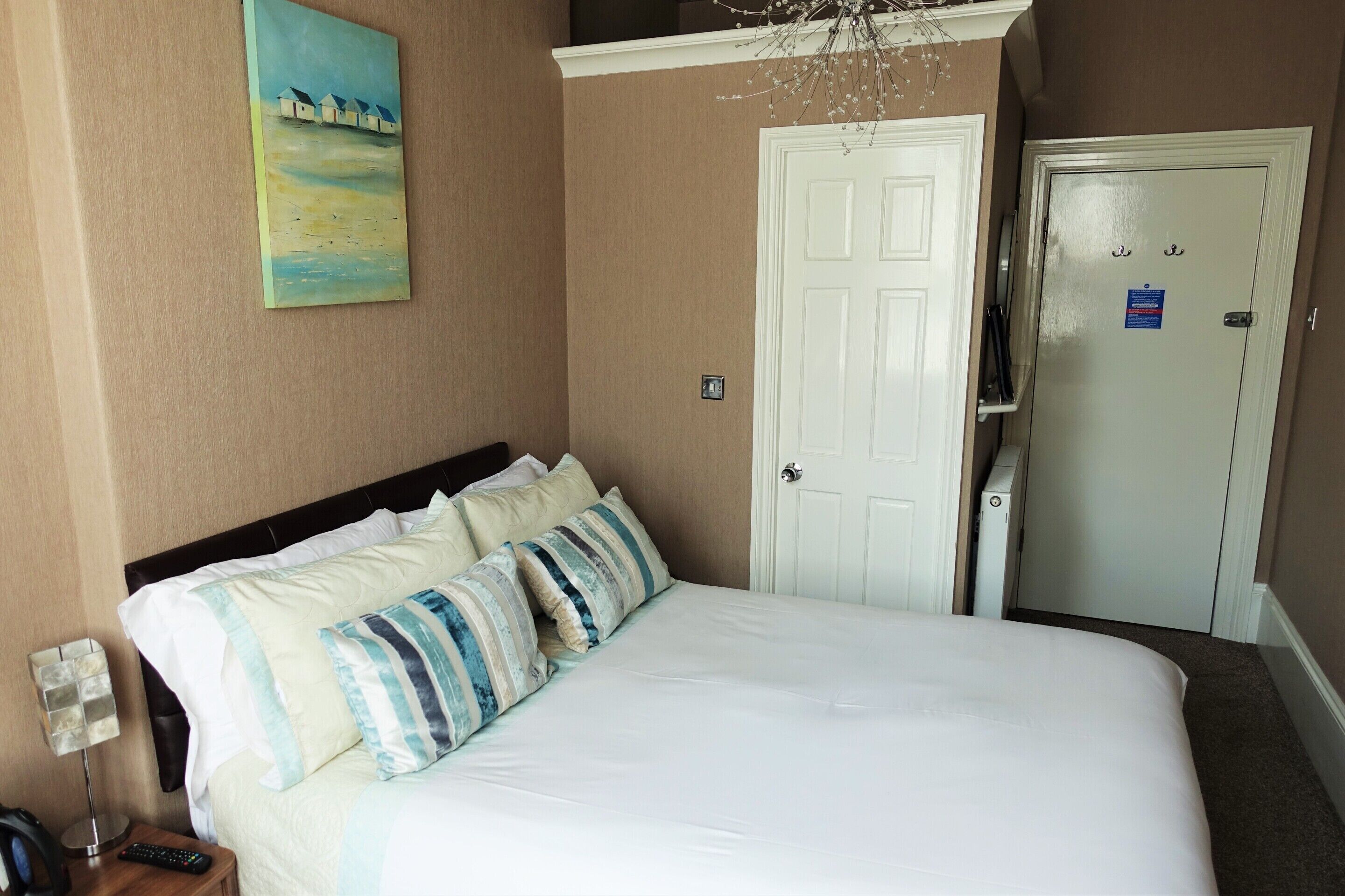 A hotel room with a bed, a painting on the wall, a door, and a wardrobe.