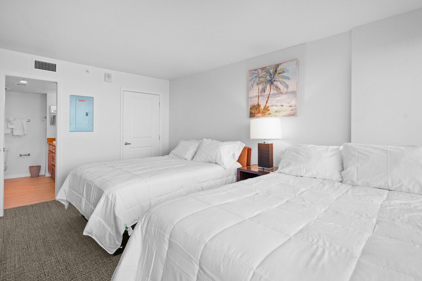 Een hotelkamer met twee bedden, een nachtkastje, een lamp en een schilderij van een strand.
