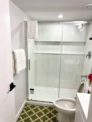 A bathroom with a glass-enclosed shower, a toilet, and a sink.