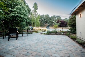 An outdoor patio area with a brick floor, two wicker chairs, and a small garden with various plants and trees. - Adorable 2-bedroom house near downtown Paso Robles (Paso Robles)