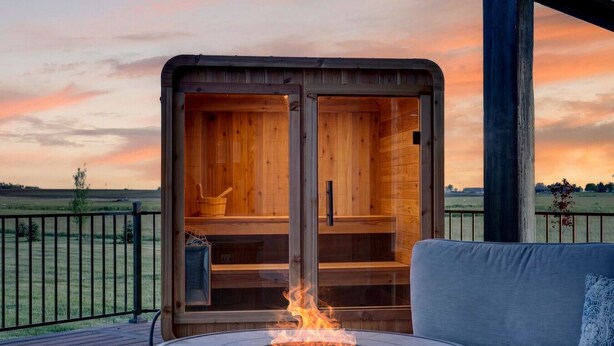 Una sauna de madera con fuego al frente, un sofá y vistas al campo.