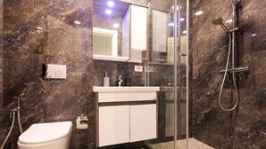 A modern bathroom with a marble wall, a glass shower enclosure, a white toilet, and a white sink with a mirror above it. - Grandstay Urban Eight (Durrës)