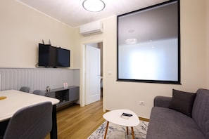 Un soggiorno moderno con una TV a schermo piatto montata a parete, un tavolino bianco e un divano grigio.