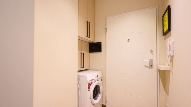 A compact laundry room with a washing machine, a microwave, and a door with a lock. - Grandstay Urban Eight (Durrës)