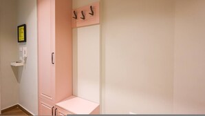 Ein Zimmer mit einem rosafarbenen Kleiderschrank, einem Kleiderhaken und einer kleinen Ablage mit einem gerahmten Zettel.