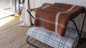 A bedroom with a bed, a bedside lamp, a door, and a chair with a blanket. - Downtown Ely Home • BWCA Gateway • Walk to Shops (Ely)