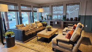 A modern living room with a leather sofa, a wooden coffee table, and a grey armchair. There are large windows with blinds, a fireplace, and a variety of plants. - Lovely 3-bedroom lodge with fitness room in Park City (Park City)