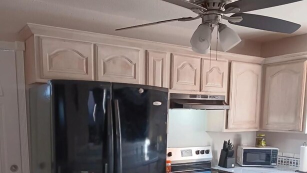 A kitchen with light wooden cabinets, a black refrigerator, a microwave, an oven, and a ceiling fan. - REALLY CUTE REMODELDED 2 BR HOME, Corpus Christi CH/A.CLOSE TO REFINERIES, I37 (Corpus Christi)