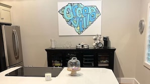 Une cuisine avec un îlot central blanc, deux tabourets, un réfrigérateur et une machine à café.