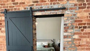 Une pièce avec un mur en briques, un lit avec des oreillers, une table de chevet et une lampe.