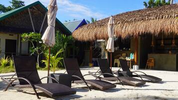 A beachside lounge with thatched umbrellas, lounge chairs, and a small bar area.