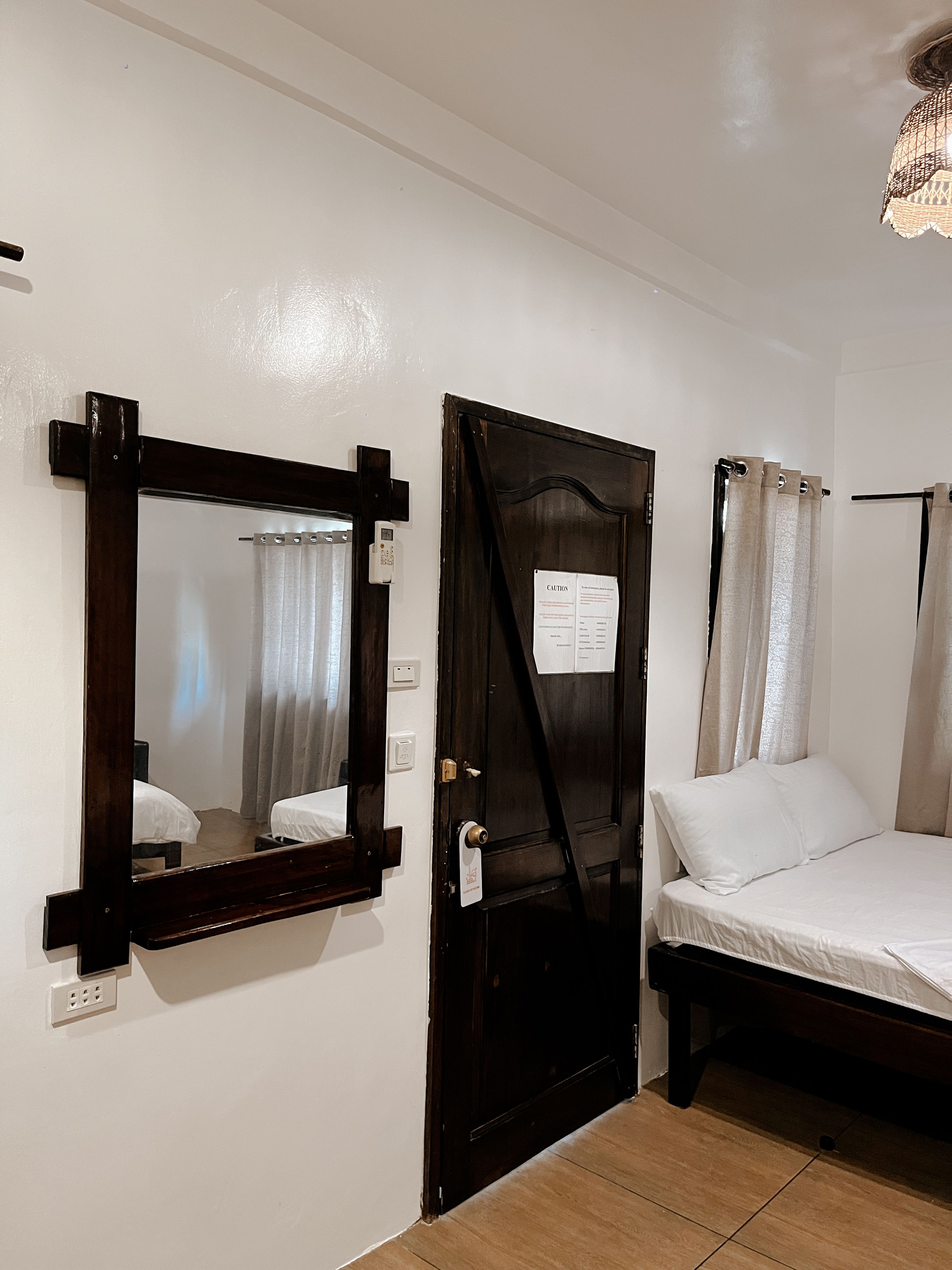 A room with a bed, a door with a sign, a mirror, and a light fixture.