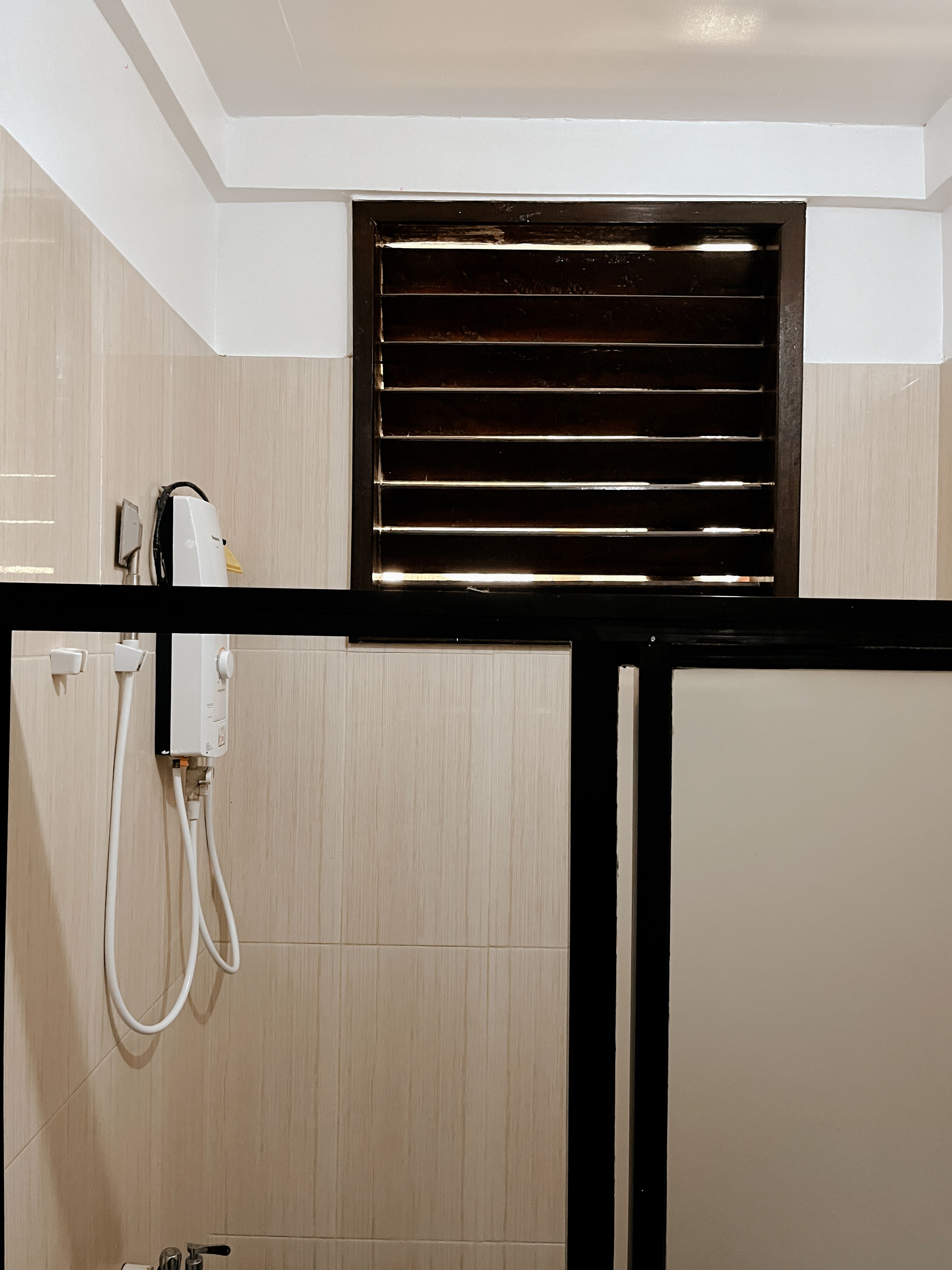 A bathroom with a shower, a towel rack, and a ventilation grille.