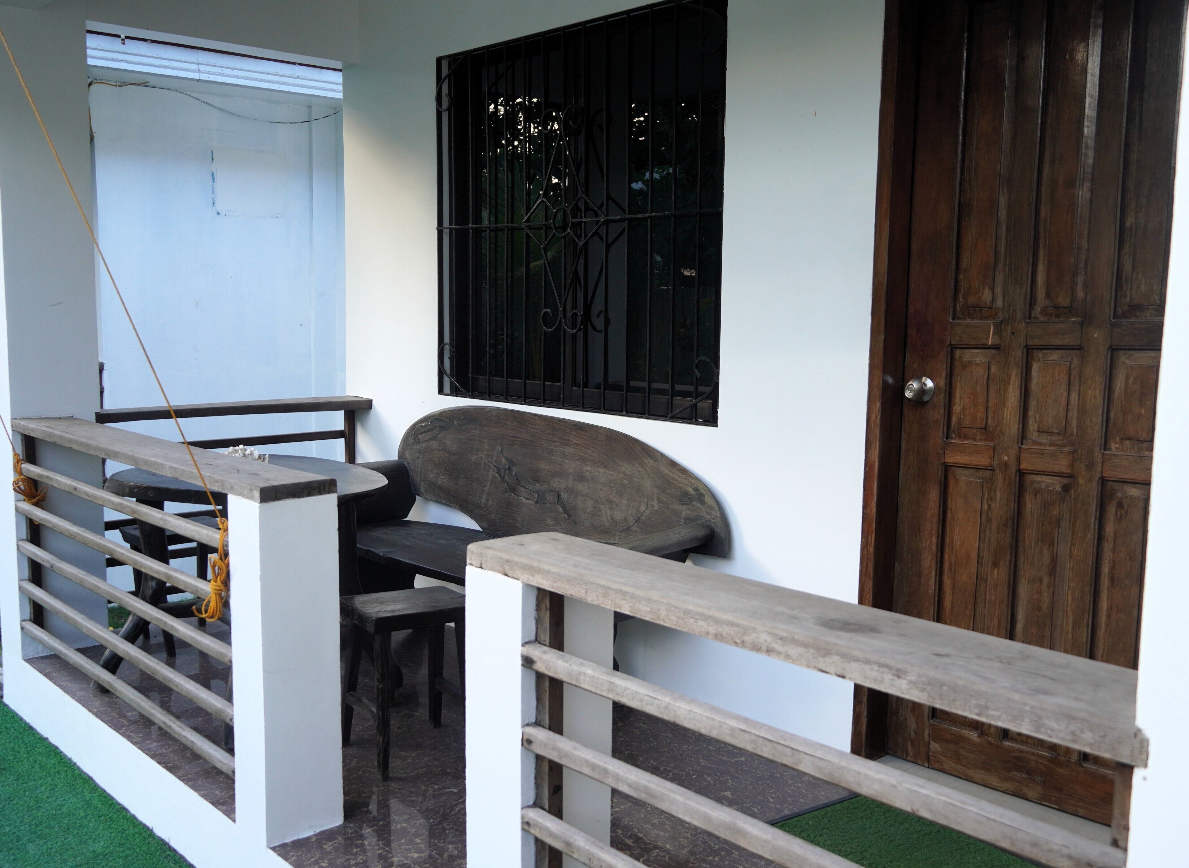 A room with a wooden door, a window with metal bars, a bench, and a small table.