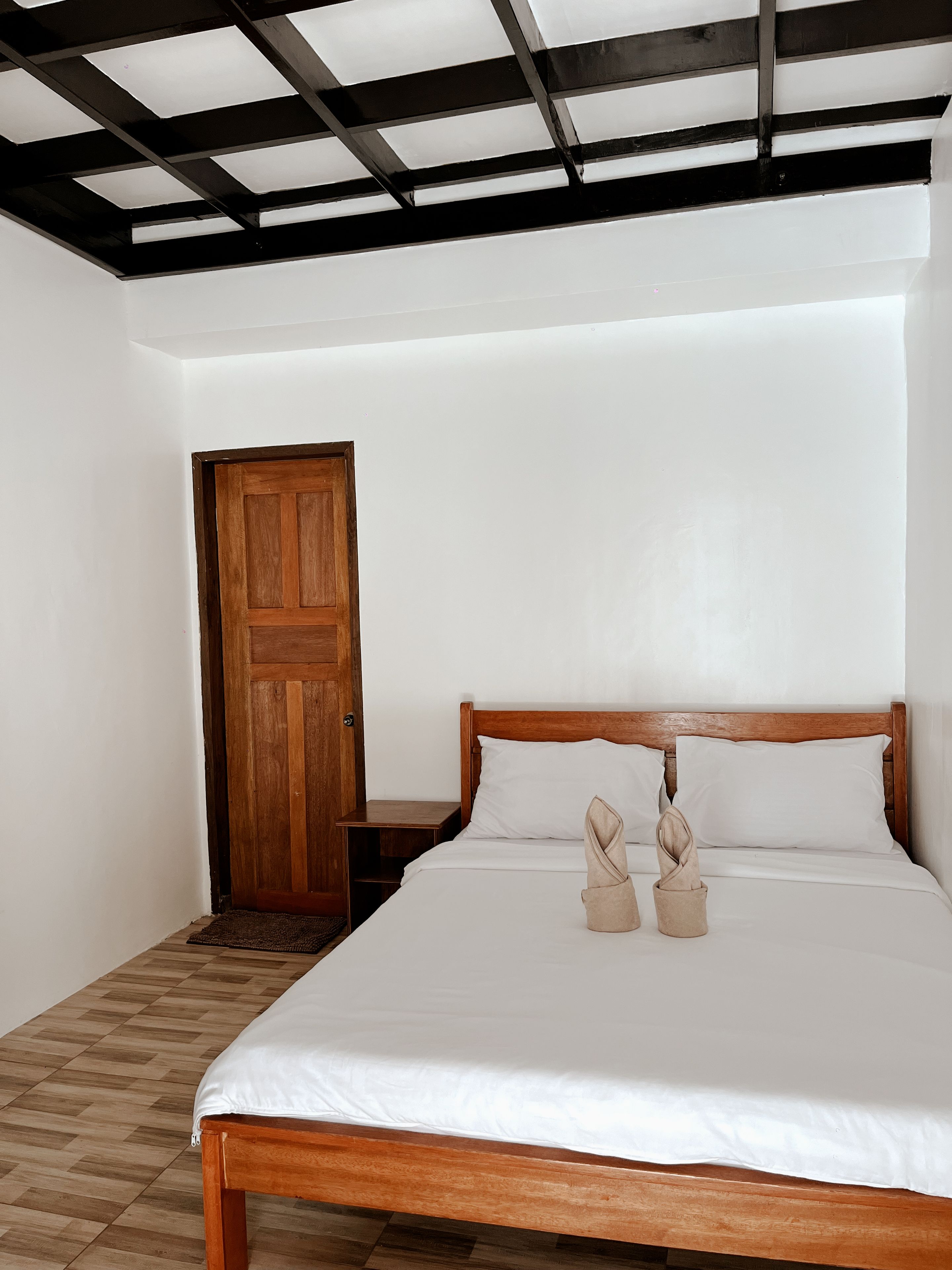 A bedroom with a wooden bed, white bedding, a wooden nightstand, and a door.