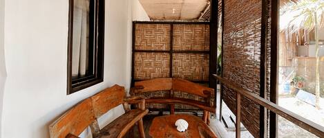 A wooden bench and table set on a veranda with a woven ceiling and a view of the outdoors.