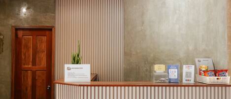 Una recepción con mostrador de madera, una planta en la barra y una pared con persianas verticales.