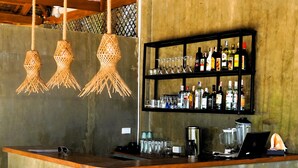 Zona de bar con taburetes, una barra, luces colgantes y una estantería con botellas y vasos.