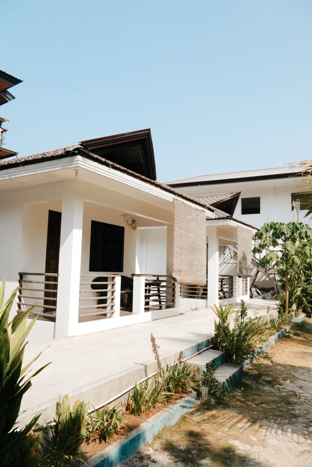 A modern residential building with a covered porch, a staircase, and a garden area with plants.