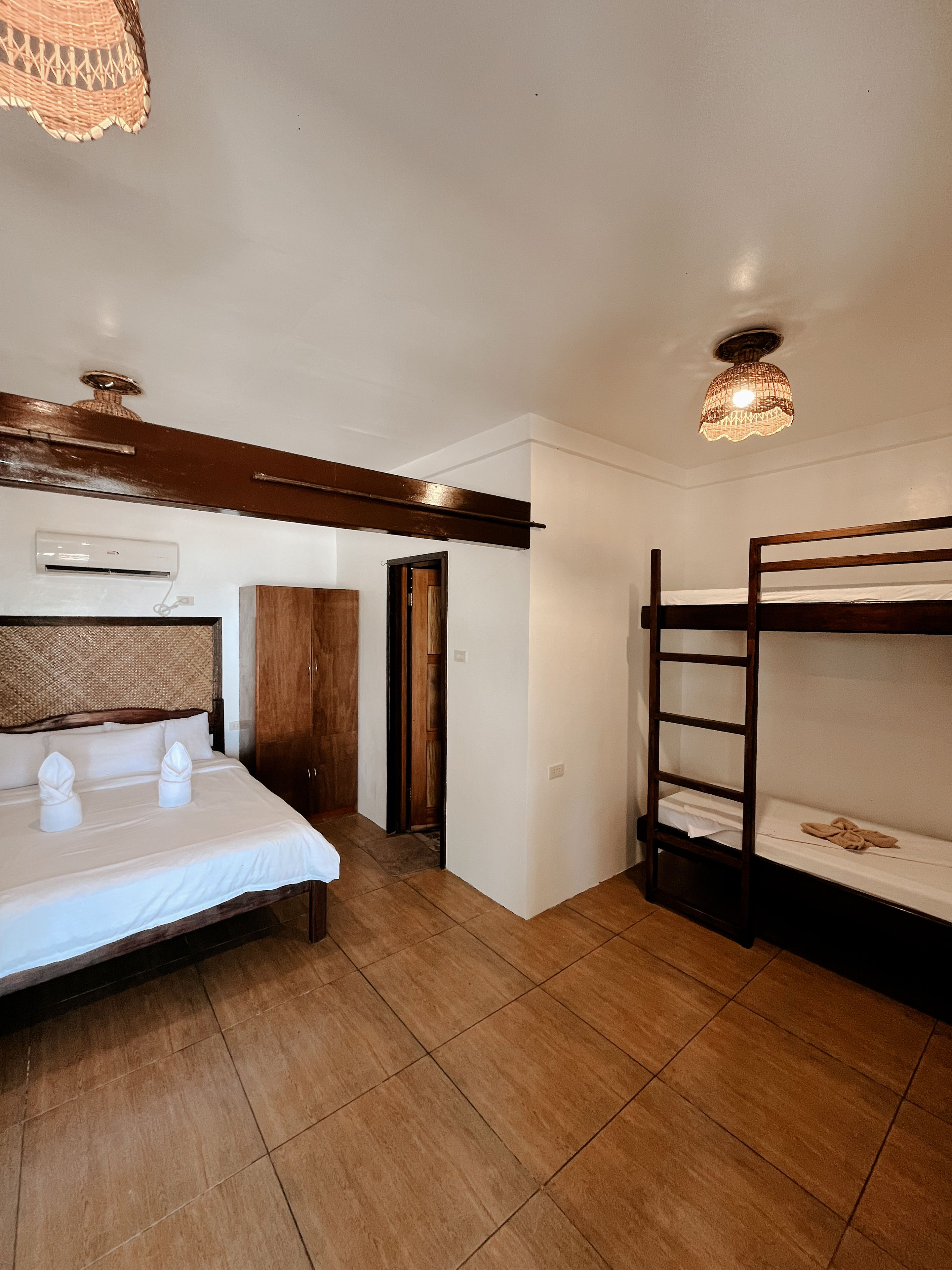 A bedroom with a bed, a bunk bed, a wooden wardrobe, and a ceiling light fixture.