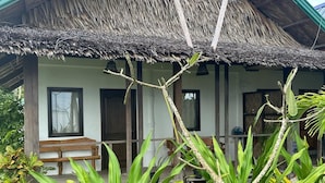 Una casa con techo de paja, un porche de madera y un jardín con plantas tropicales.