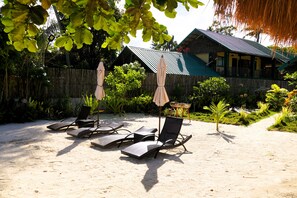 A beachside area with lounge chairs and umbrellas, a wooden fence, and a building with a green roof. - Aggehanan Beach Resort (General Luna)