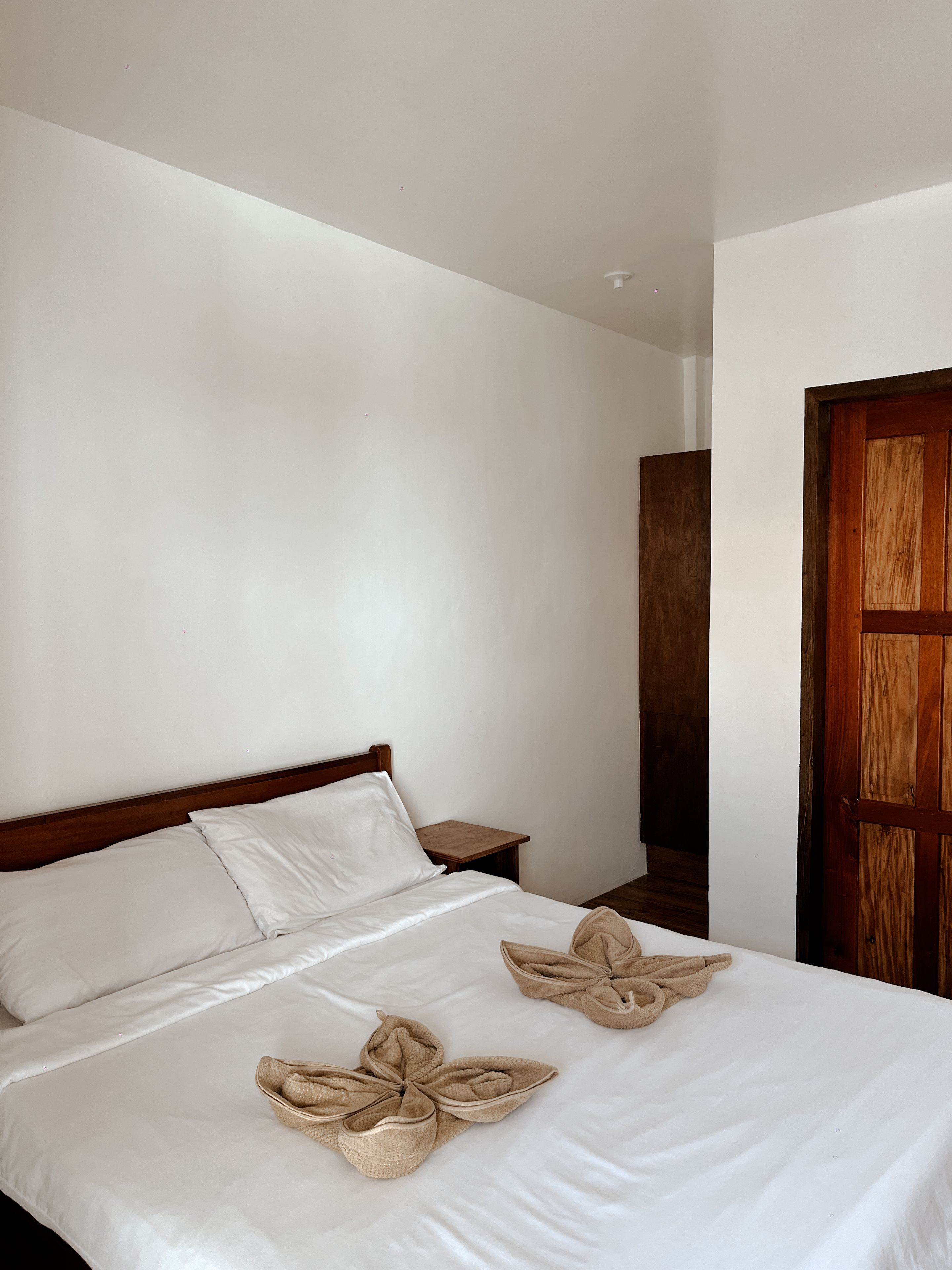 A hotel room with a single bed, a wooden headboard, a wooden nightstand, and a wooden door.