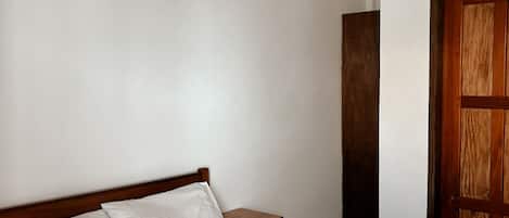 A hotel room with a single bed, a wooden headboard, a wooden nightstand, and a wooden door.