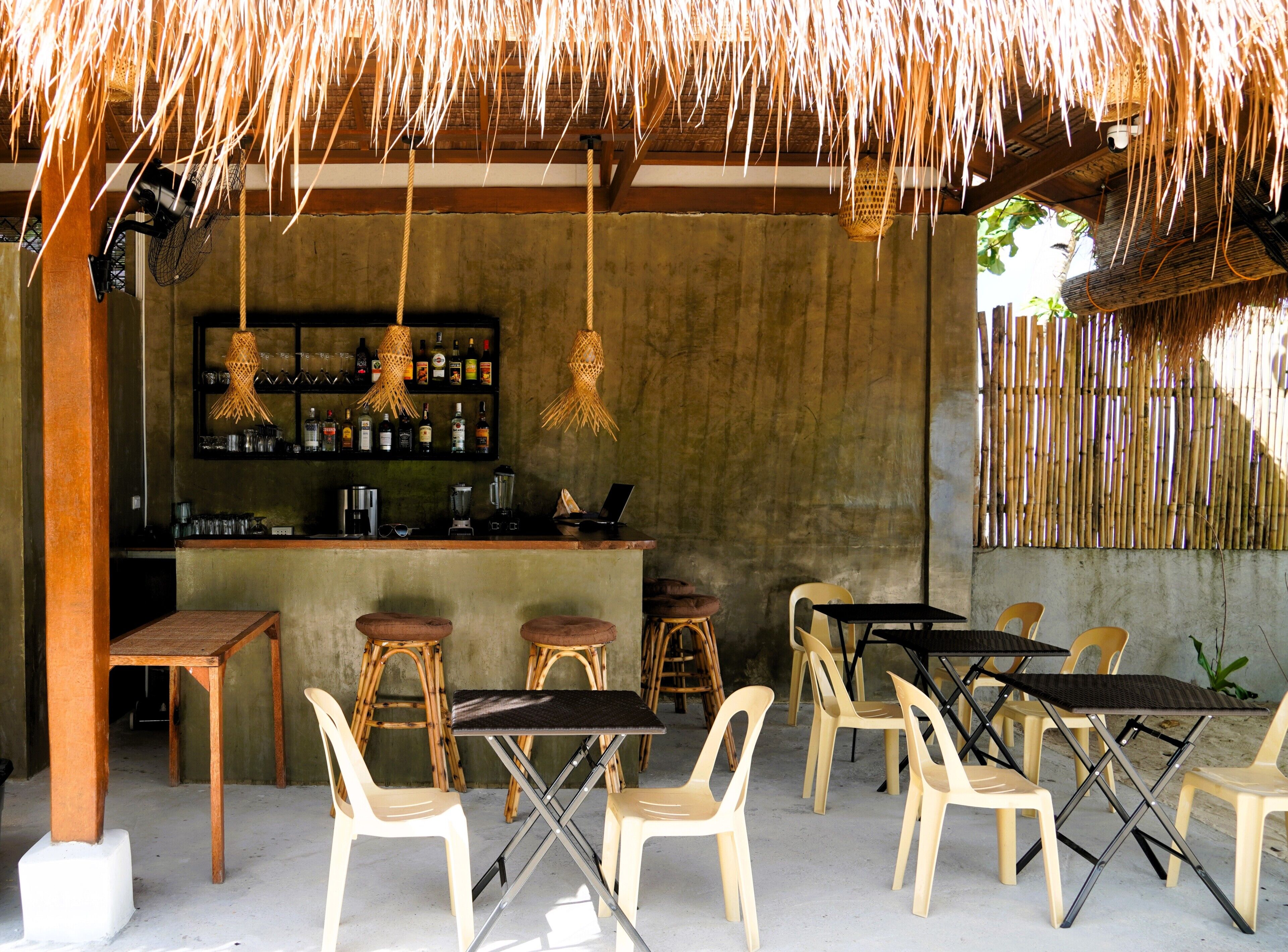 A bar area with stools, tables, and a concrete wall with a shelf of bottles.
