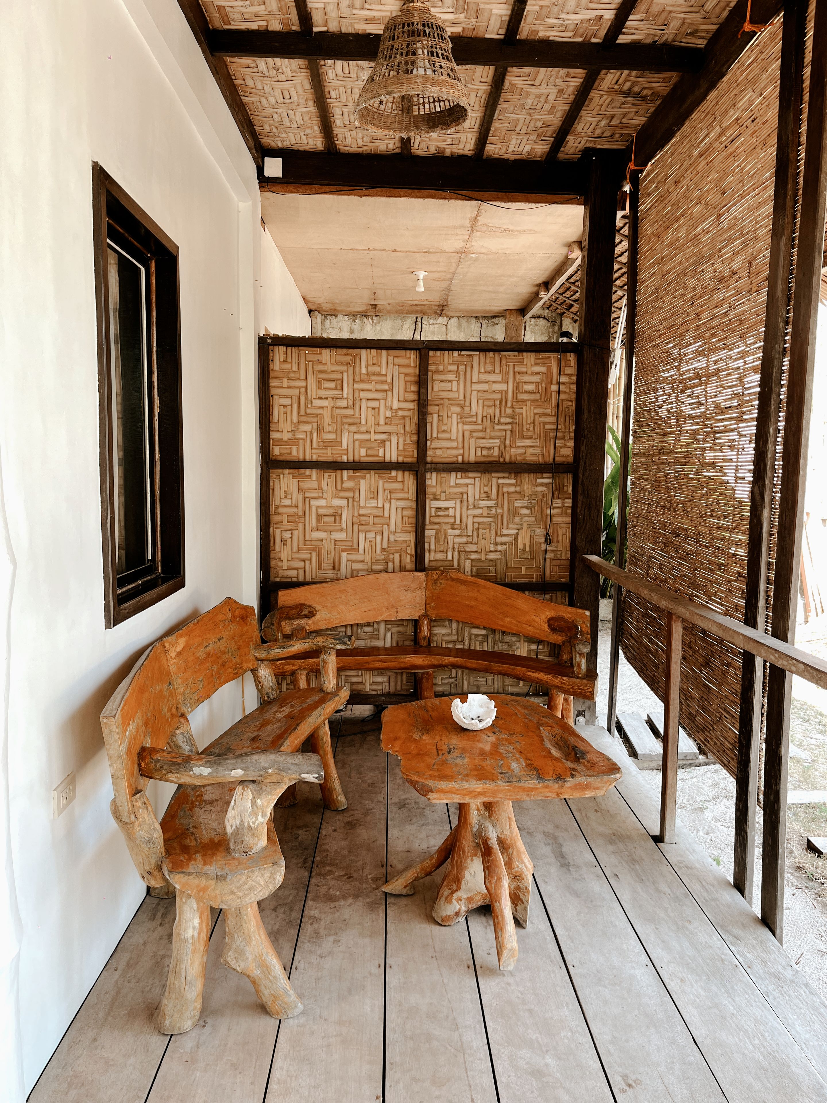 A rustic wooden bench and table set in a covered outdoor area with a woven ceiling and walls.