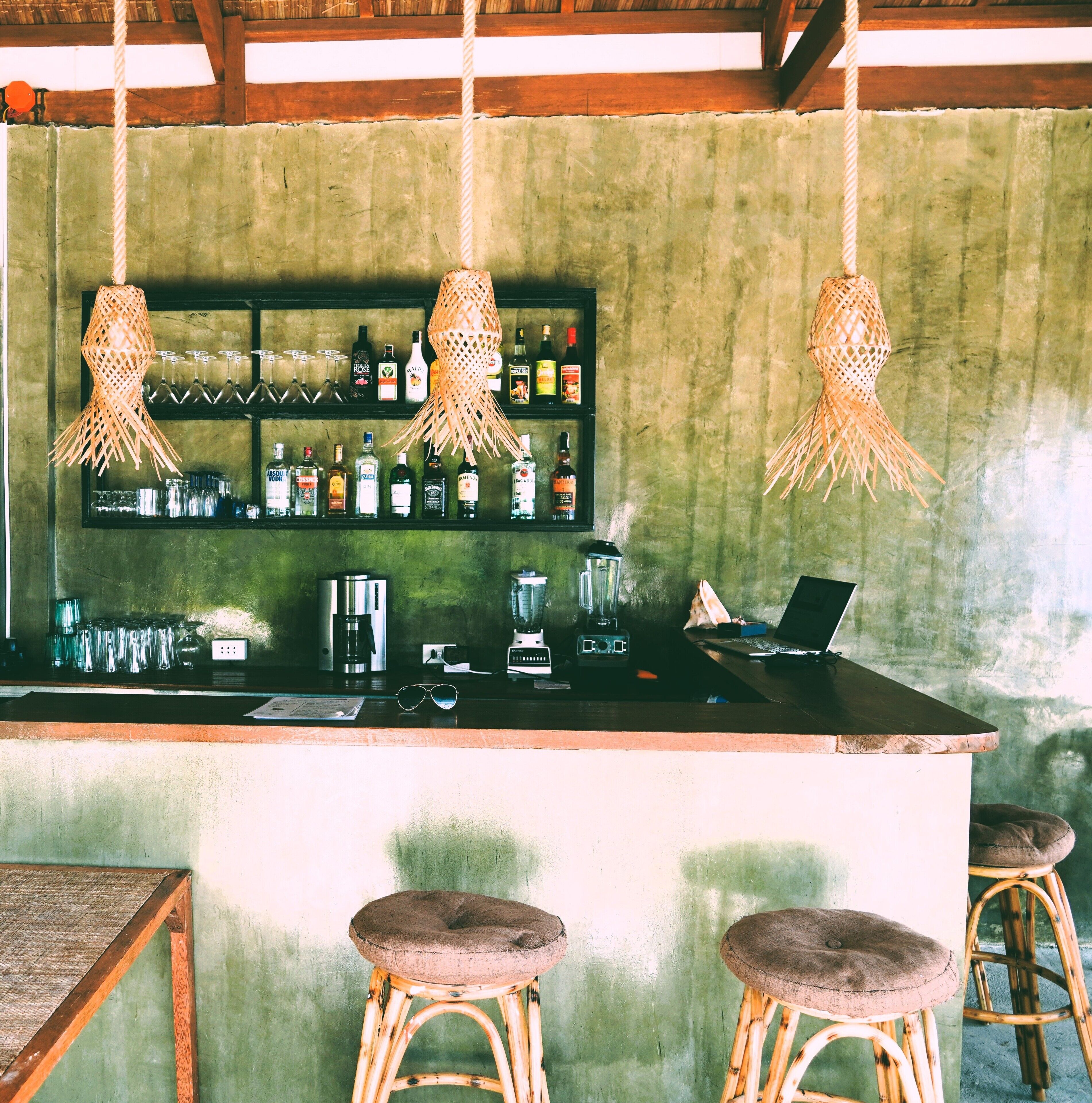 Un'area bar con un bancone, sgabelli, lampade a sospensione e uno scaffale con bottiglie.