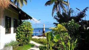 Un resort tropical con una cabaña de techo de paja, palmeras, un camino que lleva a la playa y vista al océano.