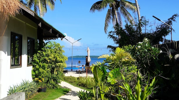 A tropical resort with a thatched-roof building, palm trees, a pathway leading to the beach, and a view of the ocean. - Aggehanan Beach Resort (General Luna)